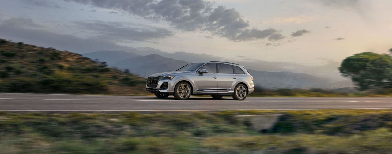 A silver 2025 Audi Q7 driving on a cloudy day.